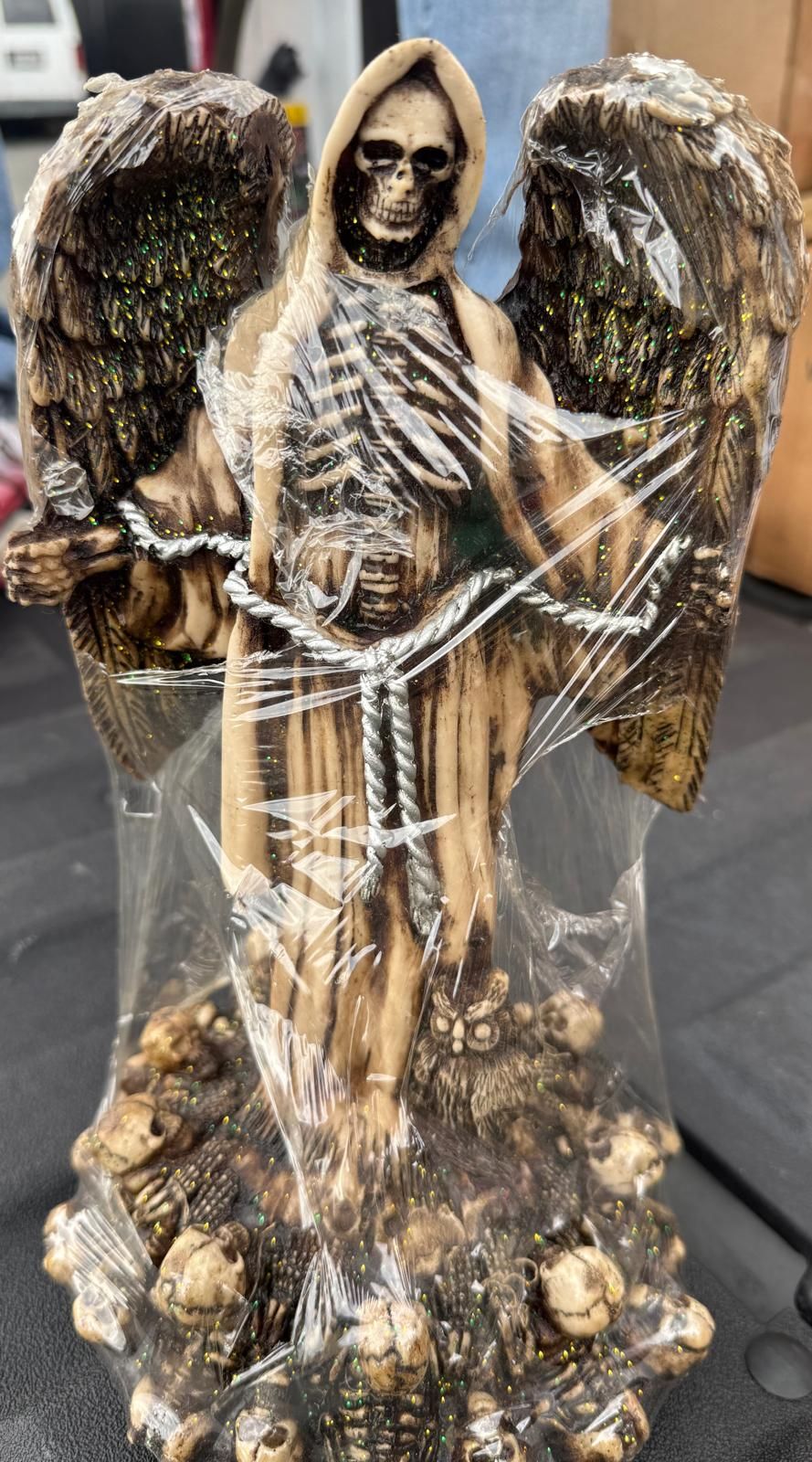 Figura esotérica de la Santa Muerte con alas de ángel extendidas, túnica beige y base decorada con calaveras y un búho.